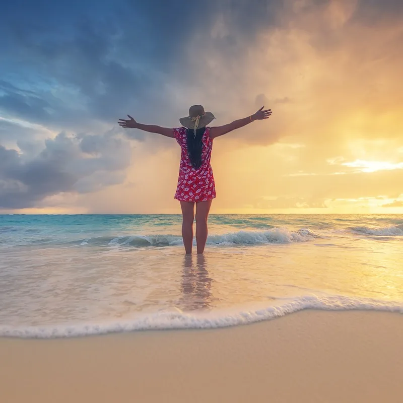 A female traveler with outstretched arms on the beach at sunset