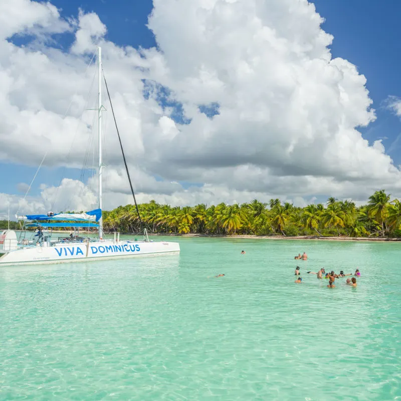 tourists in the ocean in punta cana next to a sailboat that reads "viva dominicus"