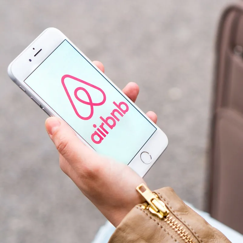 A female holding a phone with the Airbnb logo on it