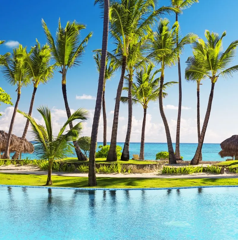 Dominican Republic resort with pool in the foreground and palm trees and ocean in the background