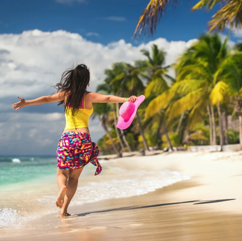 woman holding her hat running down the beach