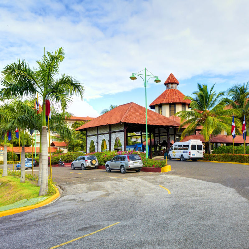 Bus and cars to the beautiful entrance of a Hotel with Palm Trees.