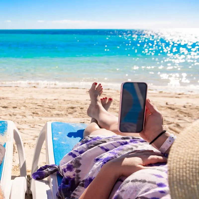 A lady on a sun lounger at the beach using her cell phone