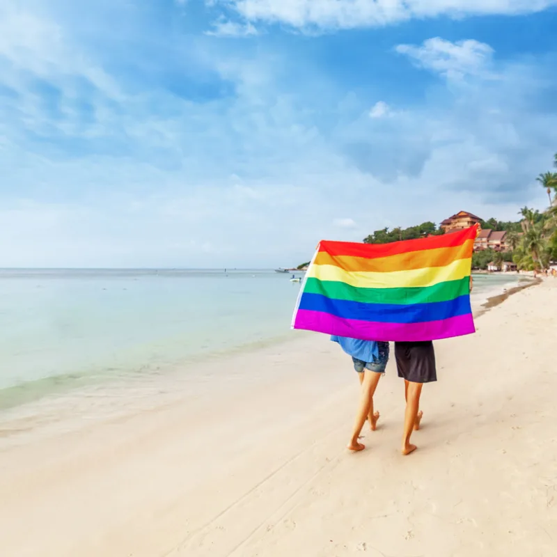 Gay travelers on a beach in the Caribbean with gay flag